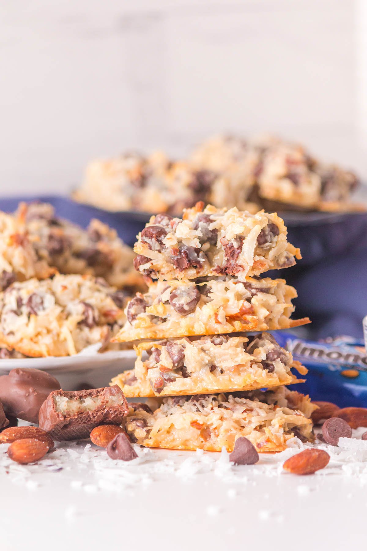 Stack of golden Almond Joy cookies with coconut shreds, chocolate chunks, and whole almonds on a white plate.