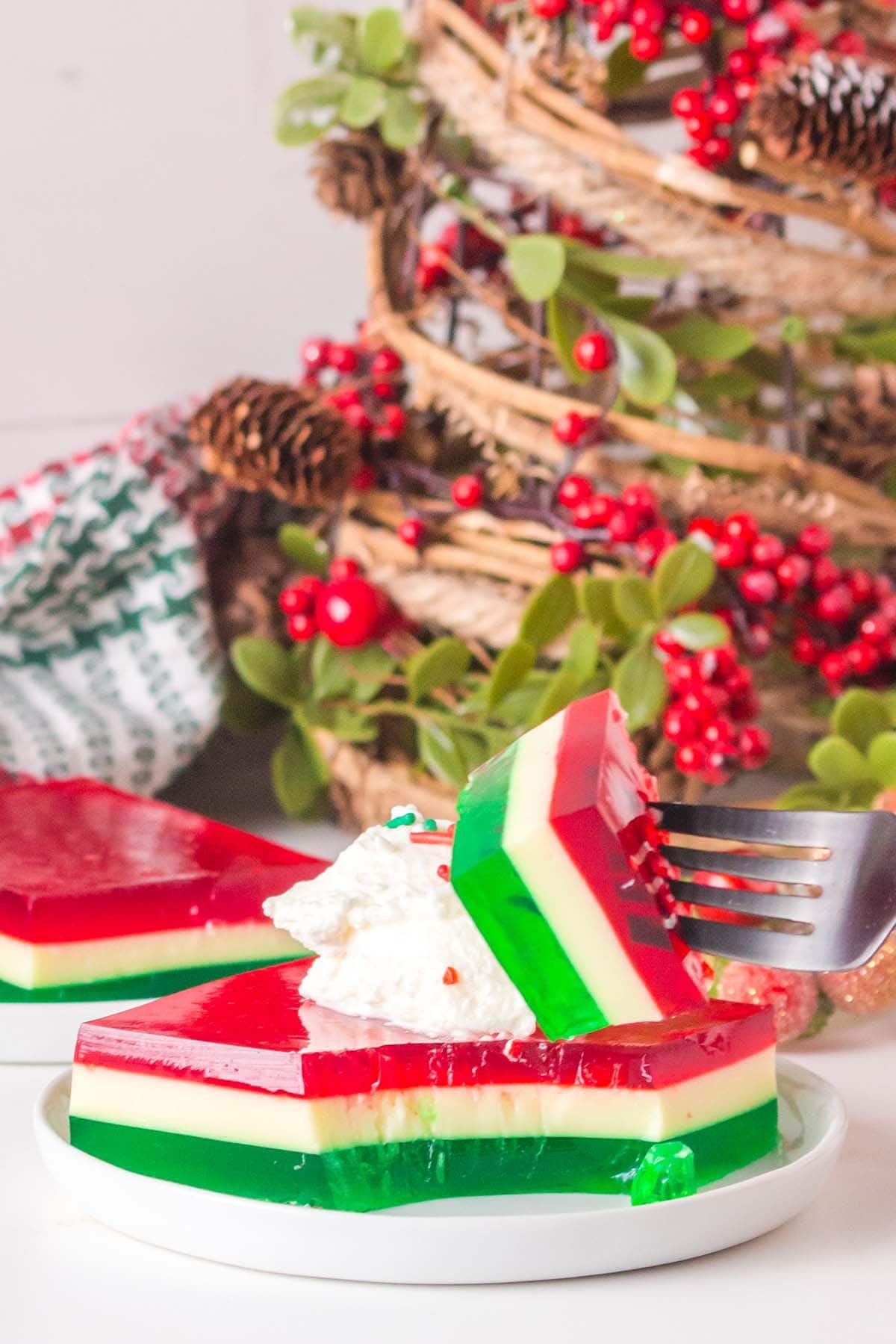 A slice of Christmas jello salad with red, white, and green layers, topped with whipped cream, on a white plate.