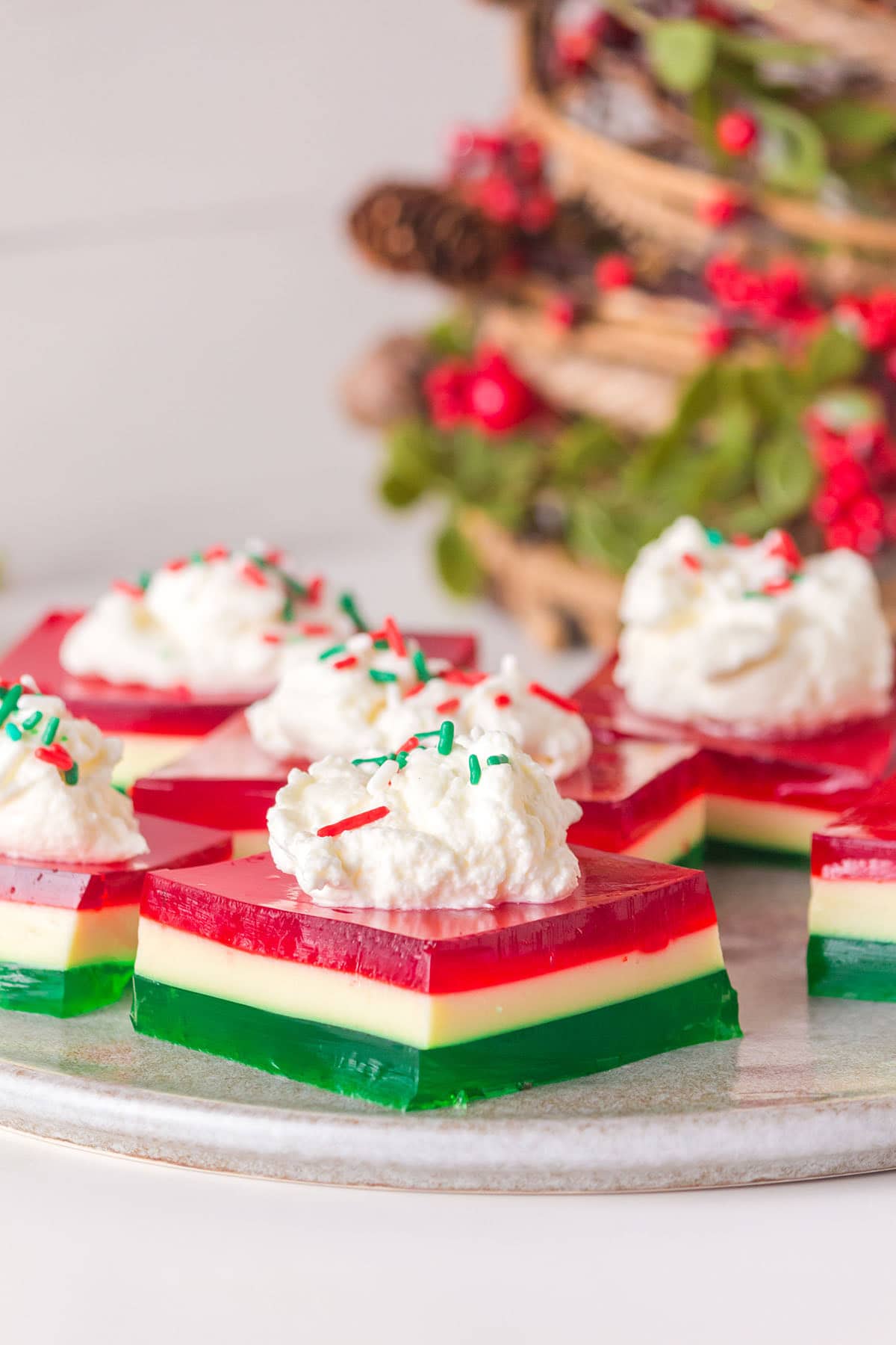 Festive Christmas jello salad in star shapes with red, white, and green layers, topped with whipped cream and colorful sprinkles.
