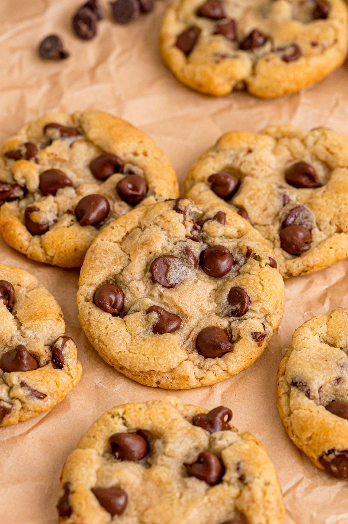 Freshly baked eggless chocolate chip cookies on parchment paper with scattered chips.