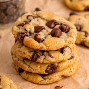 Stack of fresh eggless chocolate chip cookies on parchment paper with a jar of chips nearby.