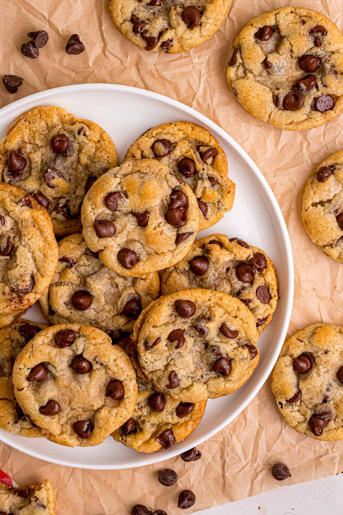 Fresh eggless chocolate chip cookies piled on a white plate over parchment paper.