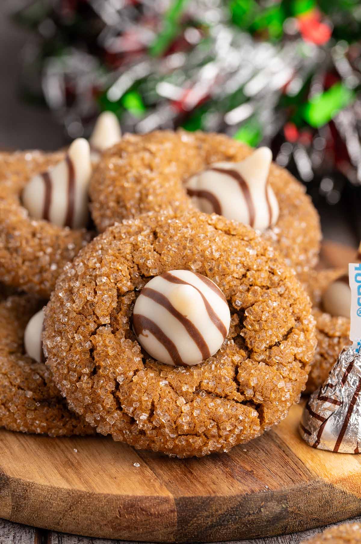 Gingerbread cookies topped with white chocolate kisses sit on a wooden board amid holiday garland.