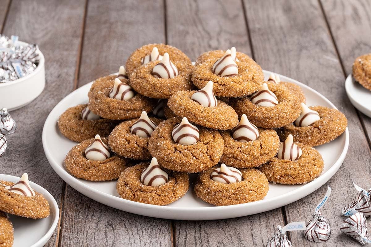 A stack of gingerbread cookies topped with chocolate kisses sits on a white plate.
