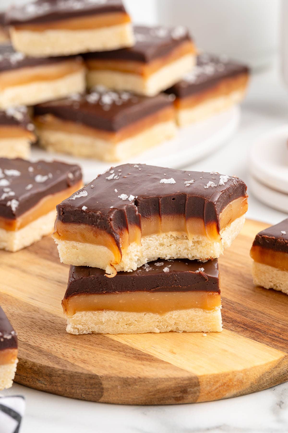 Close-up of millionaire shortbread bars with a golden shortbread base, gooey caramel layer, and dark chocolate top sprinkled with sea salt crystals.