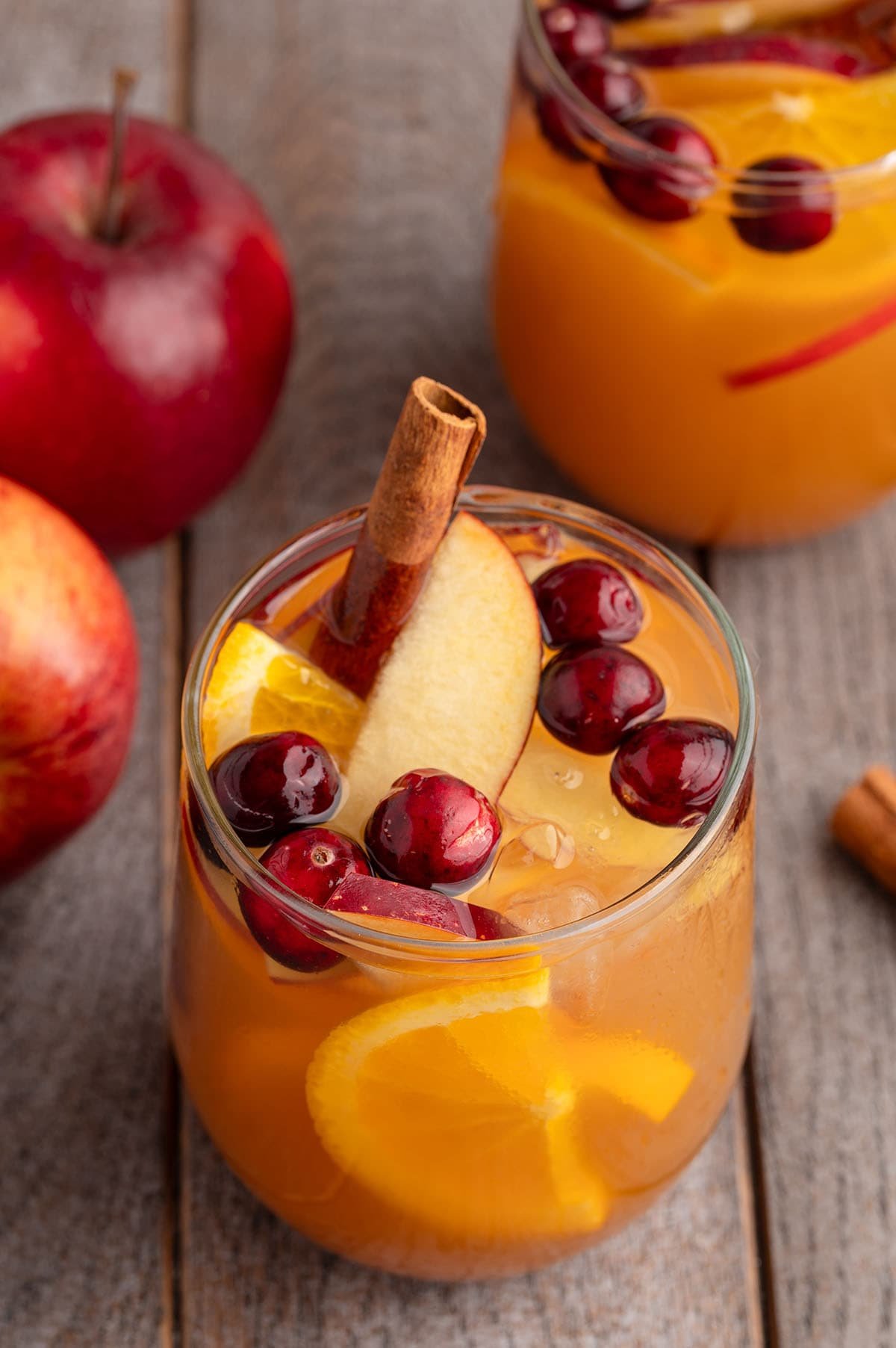 Glass of Fireball sangria packed with apple slices, orange wedges, cranberries, and cinnamon sticks on a wood table.