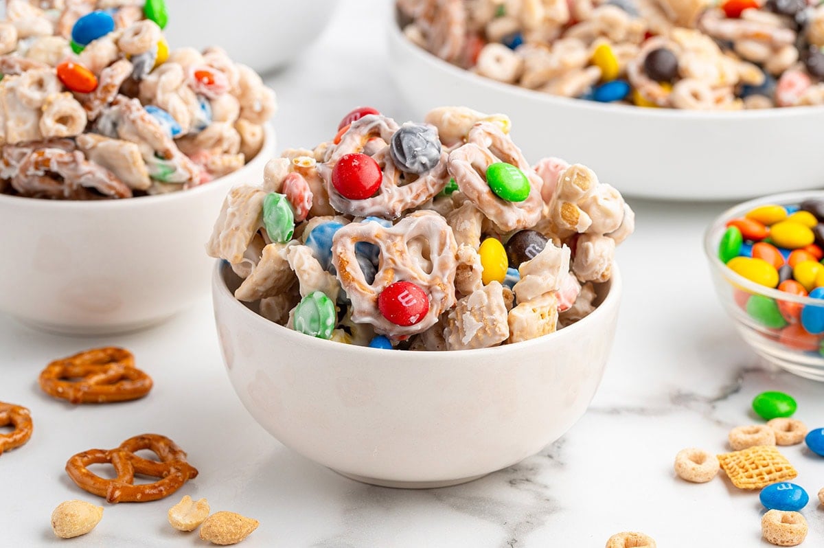 Bowl of white trash snack mix with white-coated pretzels and colorful M&Ms.