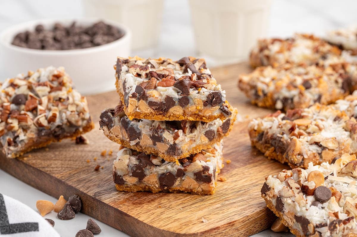 Stack of three 7-layer bars with coconut, pecans, and chocolate chips on a wood board.