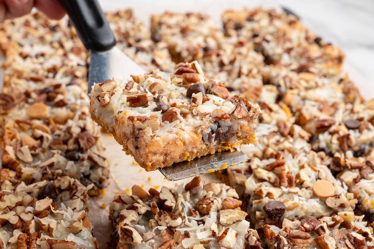 Spatula lifts a square 7-layer bar topped with coconut and pecans.