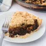 Slice of shoofly pie on a white plate with a fork stuck in the crumb topping.