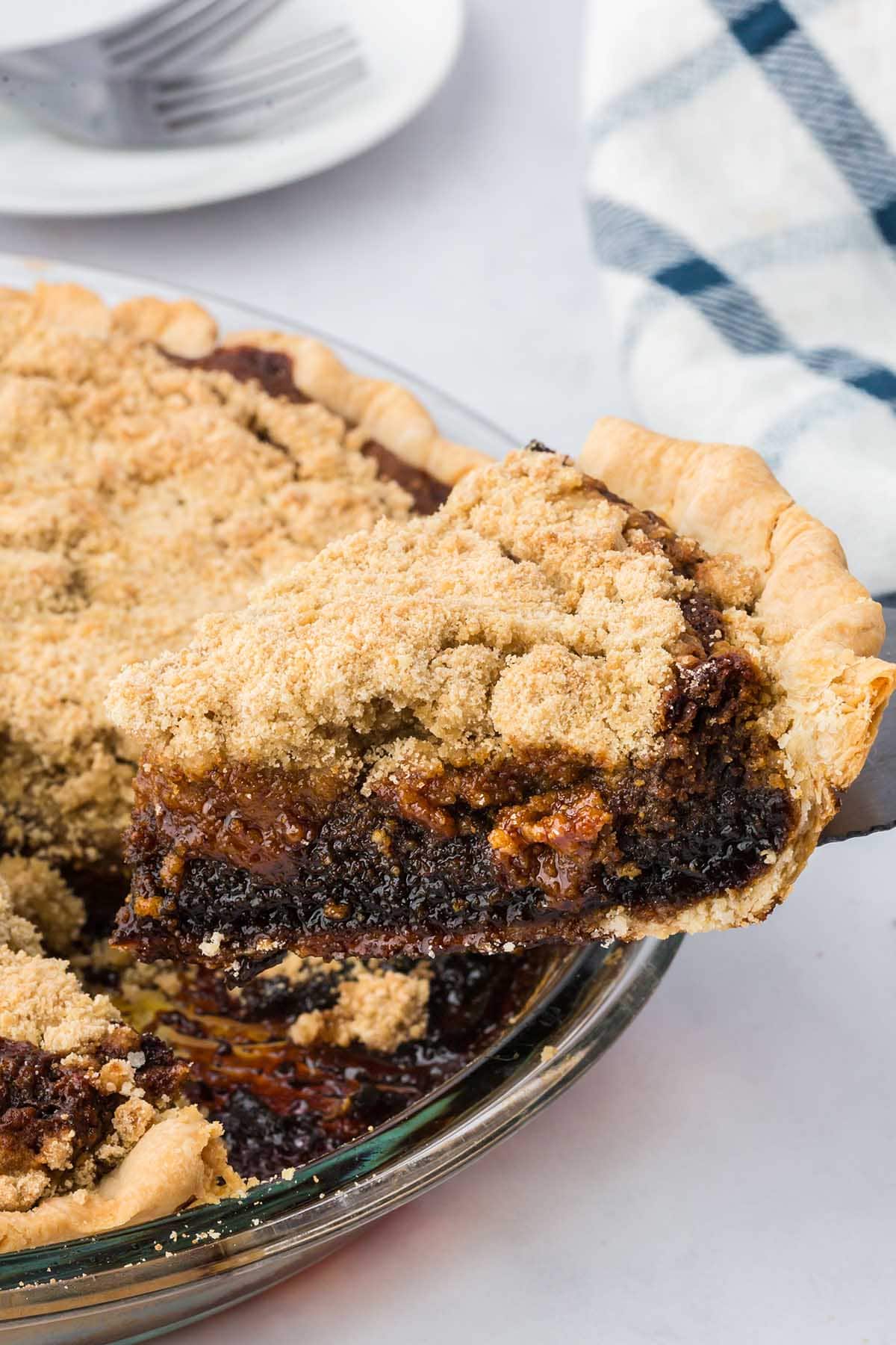 Slice of shoofly pie with crumbly topping lifted by spatula from glass dish.