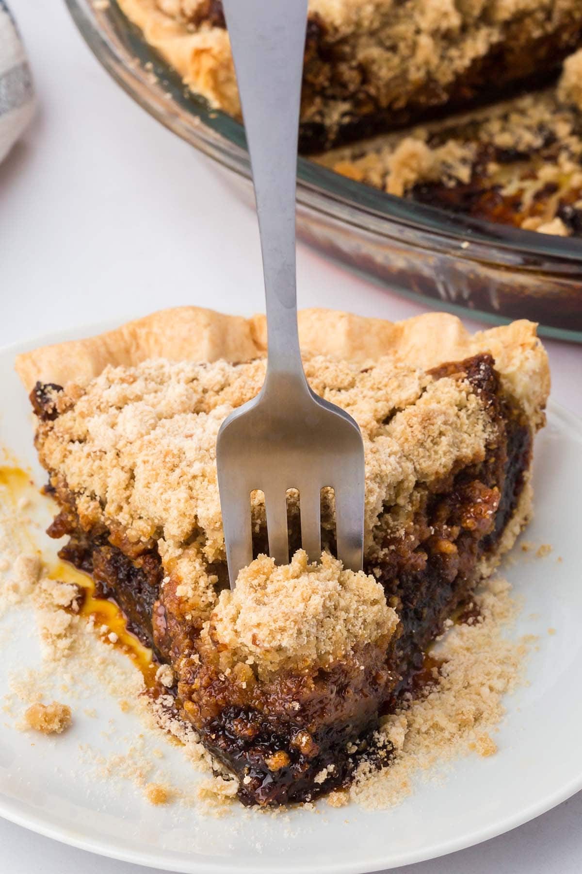 A slice of shoofly pie on a white plate with a fork stuck in the crumbly top.