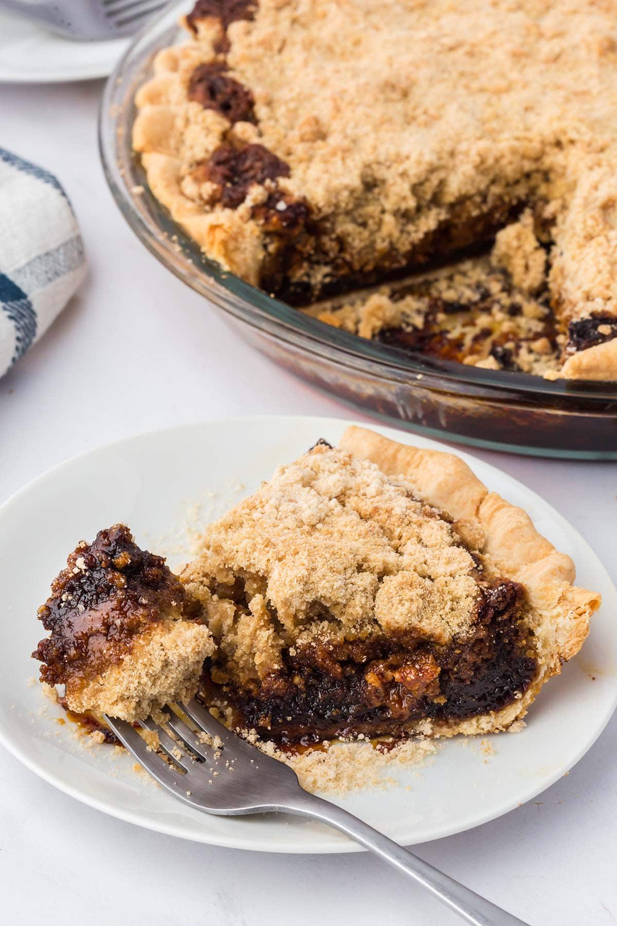 Slice of shoofly pie on a white plate with a fork ready to dig in.