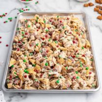 Christmas Chex Mix on a tray with red and green M&Ms, pretzels, and white chocolate bits.