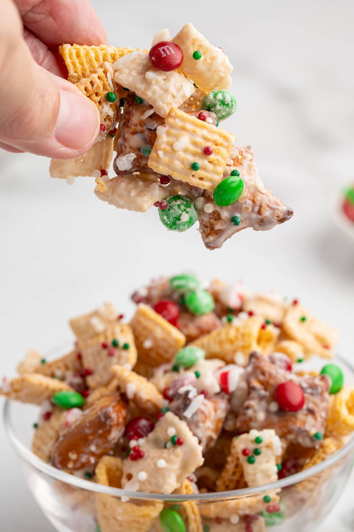 Hand grabs a gooey piece of Christmas Chex Mix with red and green M&Ms.