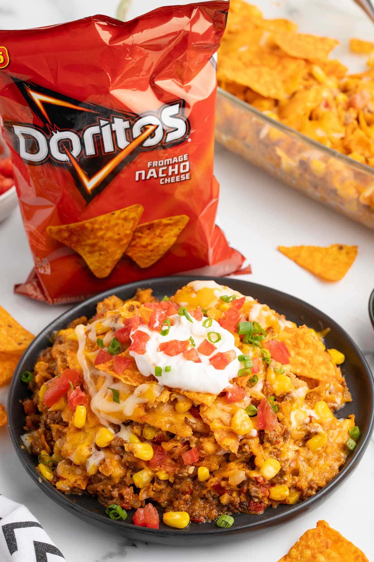 Plate of Dorito nacho cheese casserole with sour cream, tomatoes, corn, and green onions.