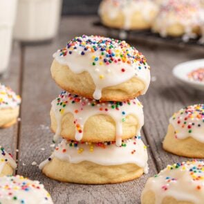 Stack of soft Italian cookies with white icing and rainbow sprinkles sits next to a glass of milk.