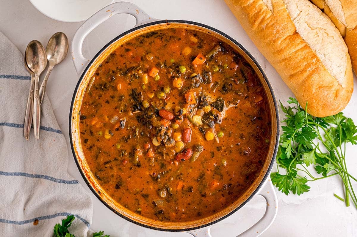 Pot of minestrone soup packed with beans, carrots, corn, and greens.
