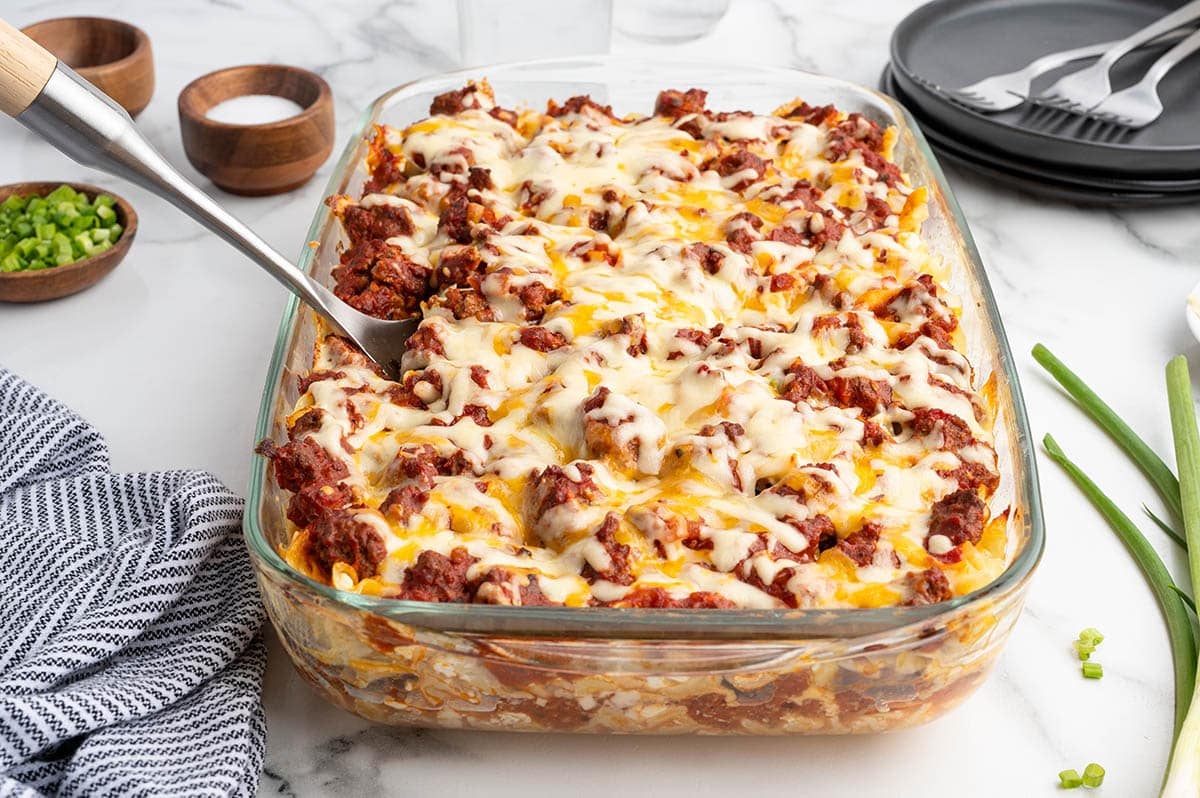 Sour cream noodle bake in a glass dish, topped with melted cheese with green onions laid beside it