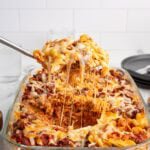 Spoon lifts gooey cheese from Sour Cream Noodle Bake casserole.