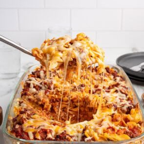Spoon lifts gooey cheese from Sour Cream Noodle Bake casserole.
