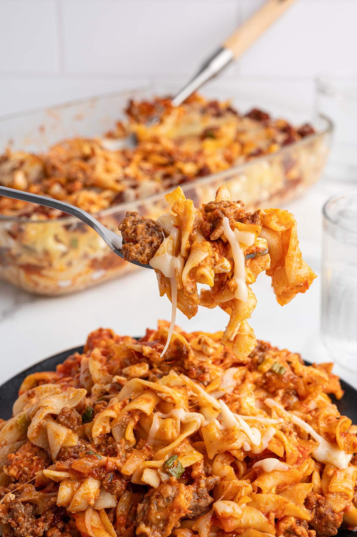 Fork scoops cheesy sour cream noodle bake from a glass dish.