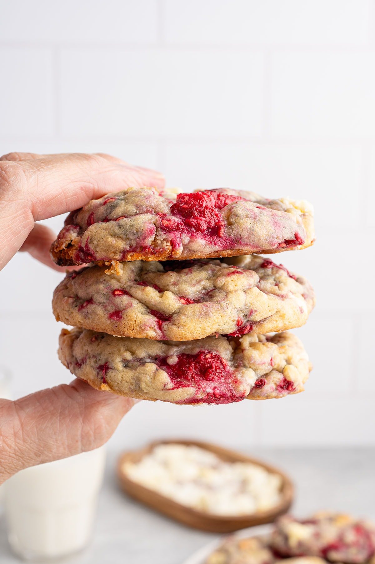 Hands hold a stack of three white chocolate raspberry cookies with red filling.