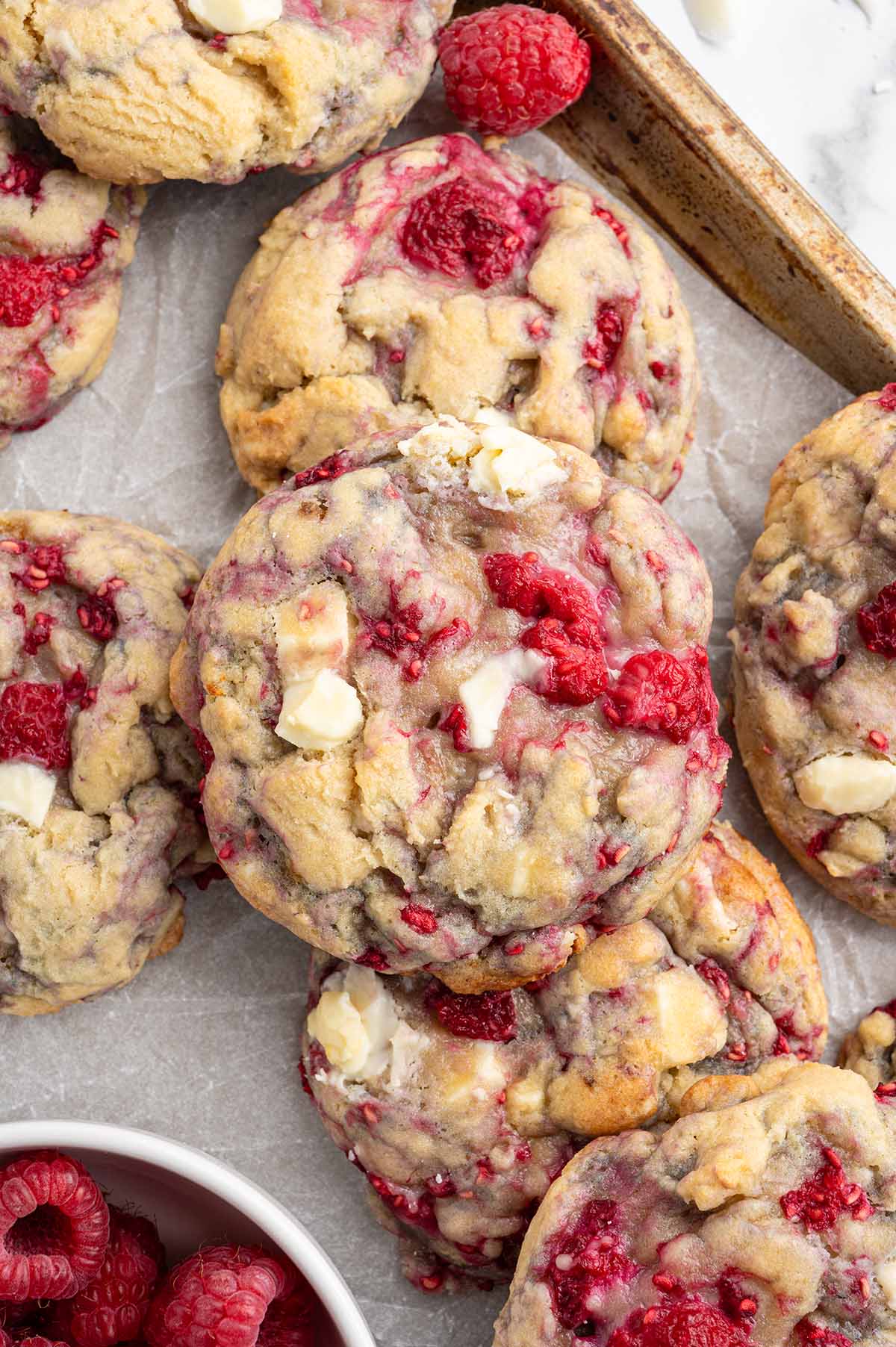 White chocolate raspberry cookies stacked on parchment paper with fresh berries nearby.
