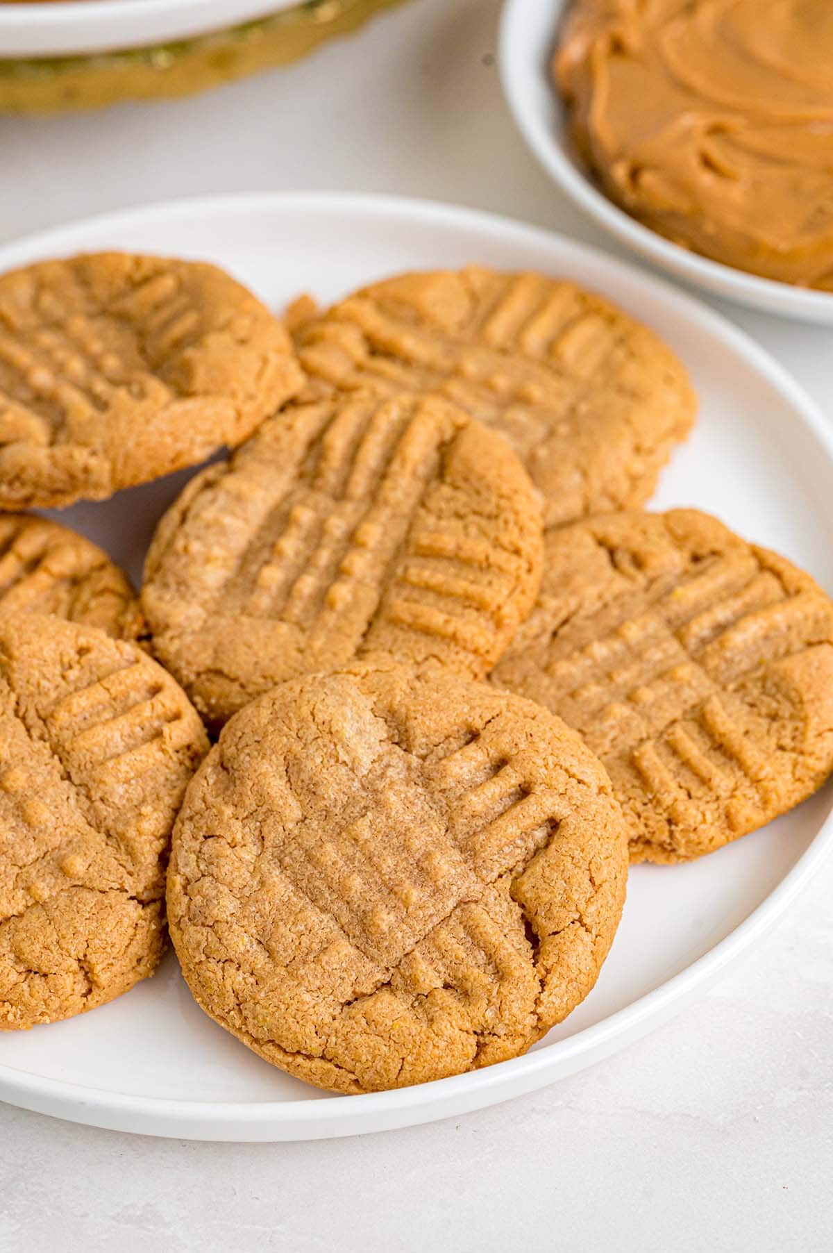 Plate of soft peanut butter cookies sits next to a bowl of creamy peanut butter.