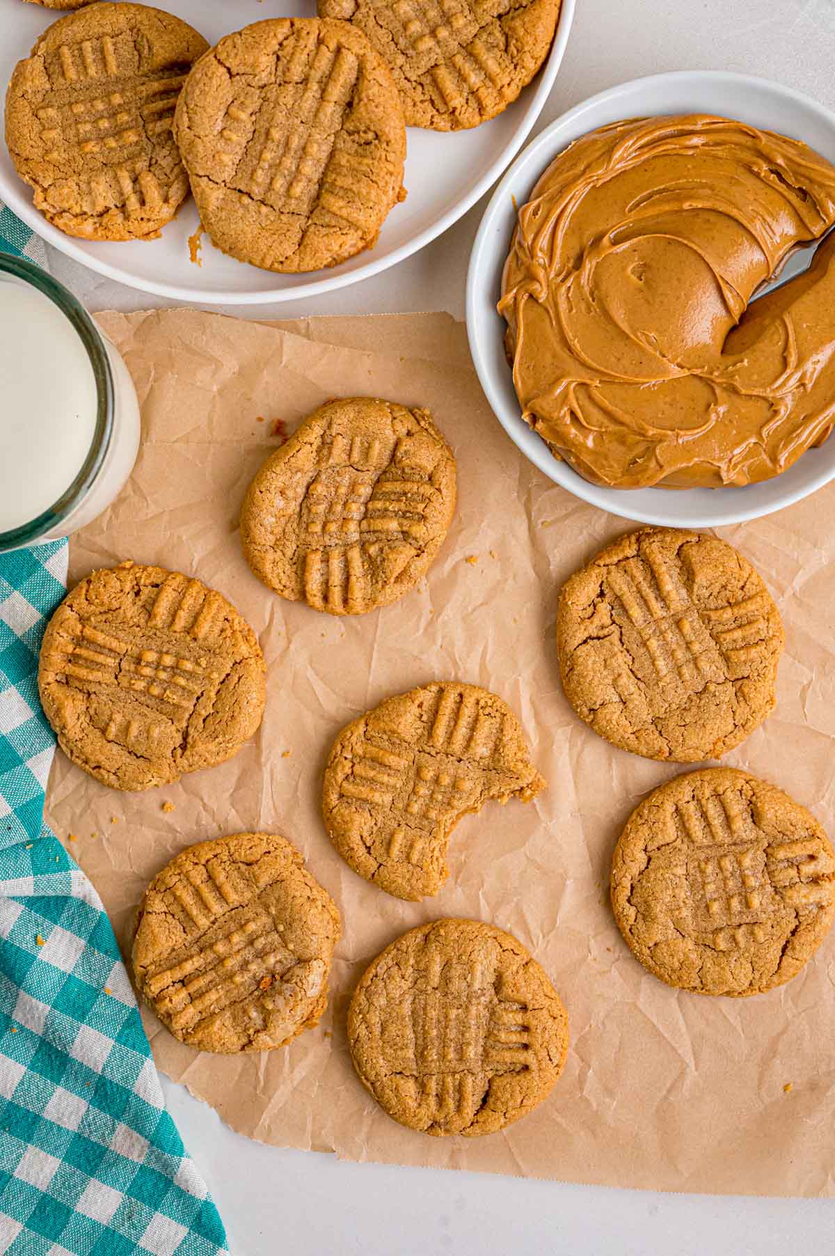 Peanut butter cookies with crosshatch tops sit next to a bowl of creamy peanut butter.