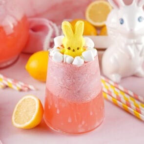 Pink Easter punch slush in a glass topped with yellow Peeps bunny and marshmallows, lemon slices around it.