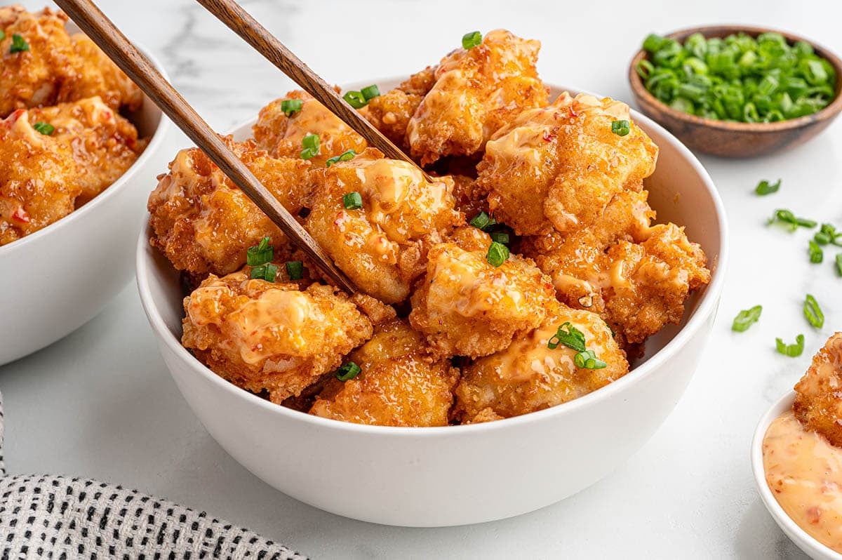 Golden crispy Bang Bang shrimp in a white bowl topped with green onions.
