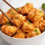 Chopsticks lift Bang Bang shrimp from bowl with orange sauce and scallions.