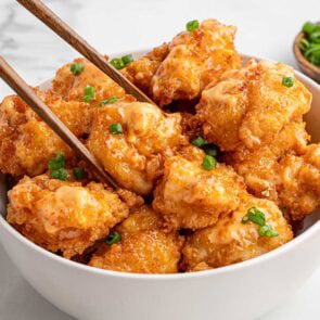 Chopsticks lift Bang Bang shrimp from bowl with orange sauce and scallions.