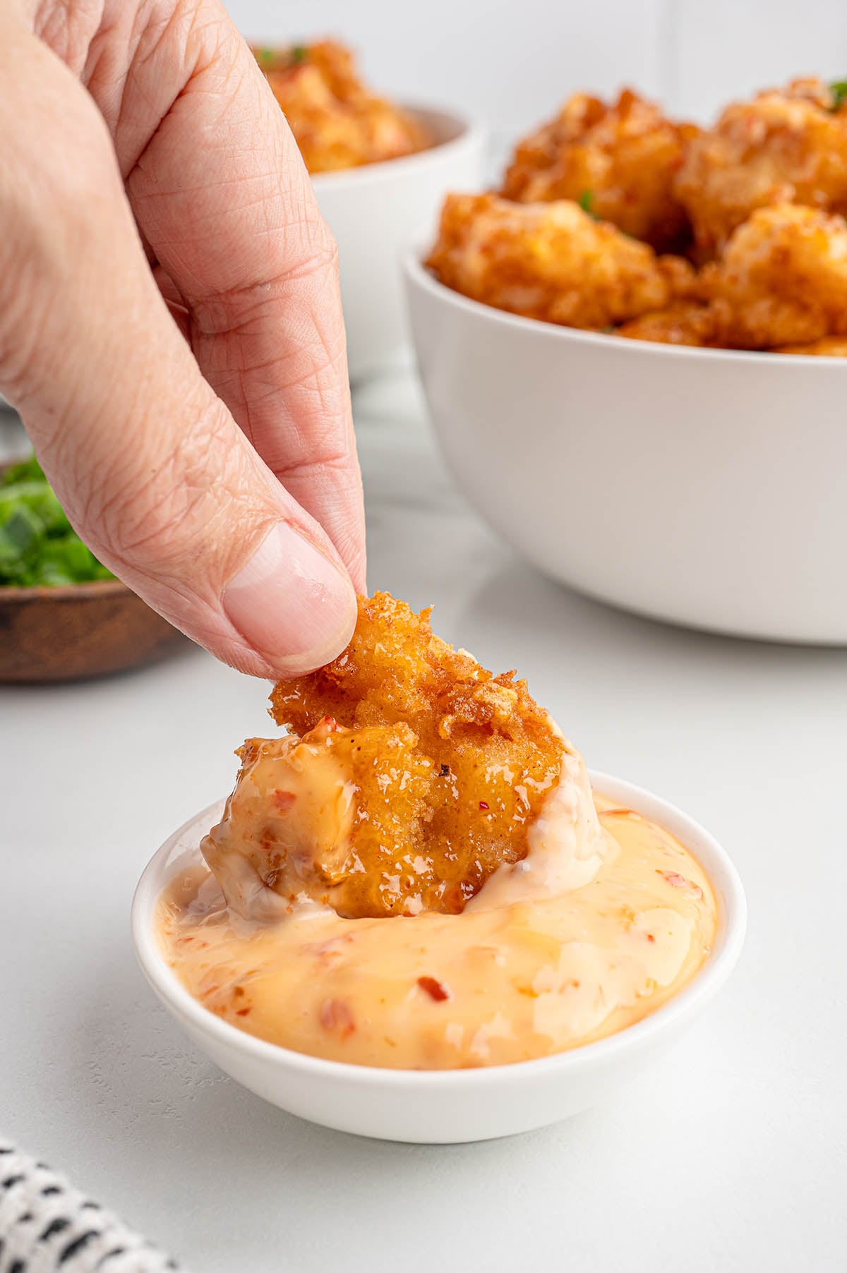 Hand holds crispy Bang Bang shrimp dipped in creamy pink sauce.