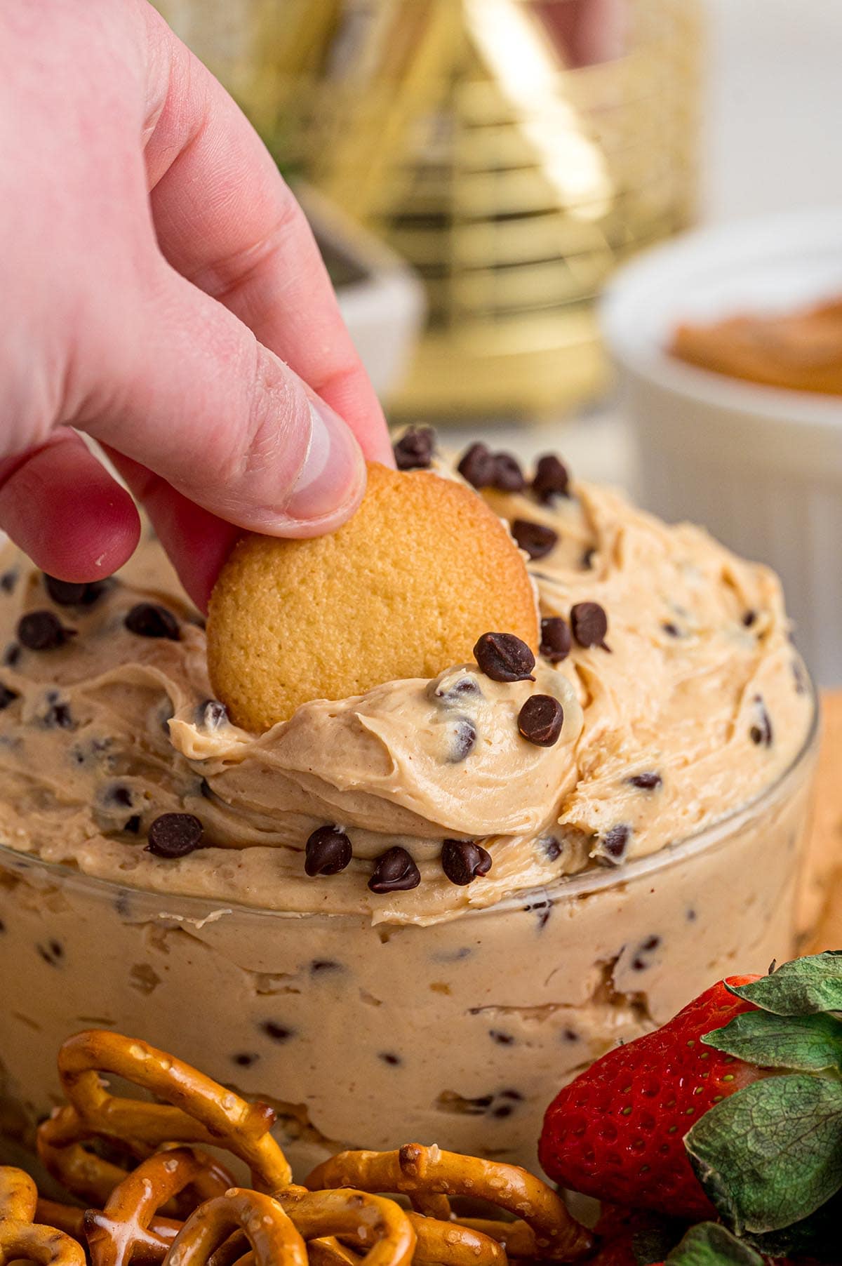 Hand dips a golden cookie into creamy buckeye dip with chocolate chips.