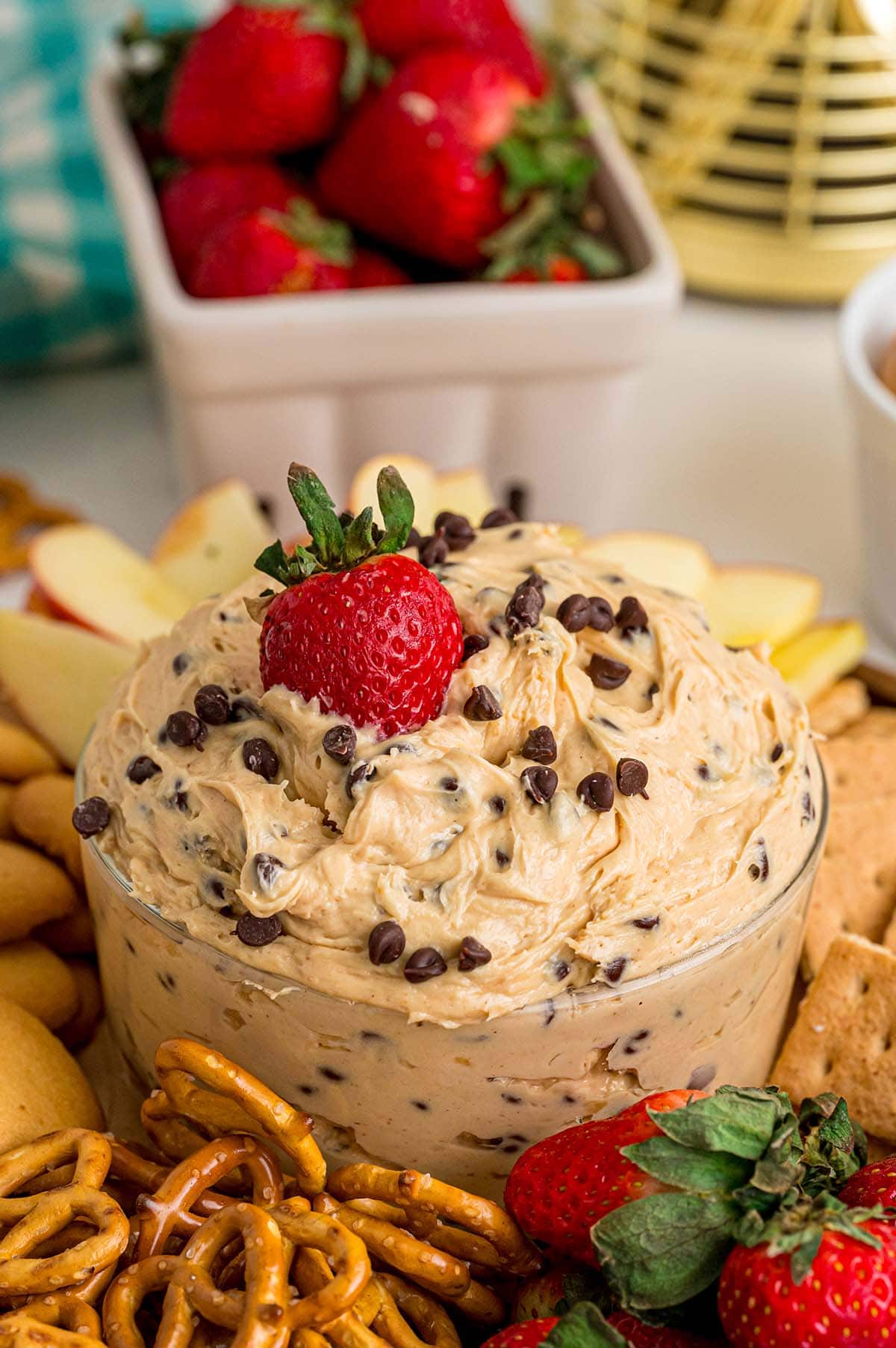 Bowl of creamy buckeye dip with chocolate chips, next to apple slices, strawberries, and pretzels.