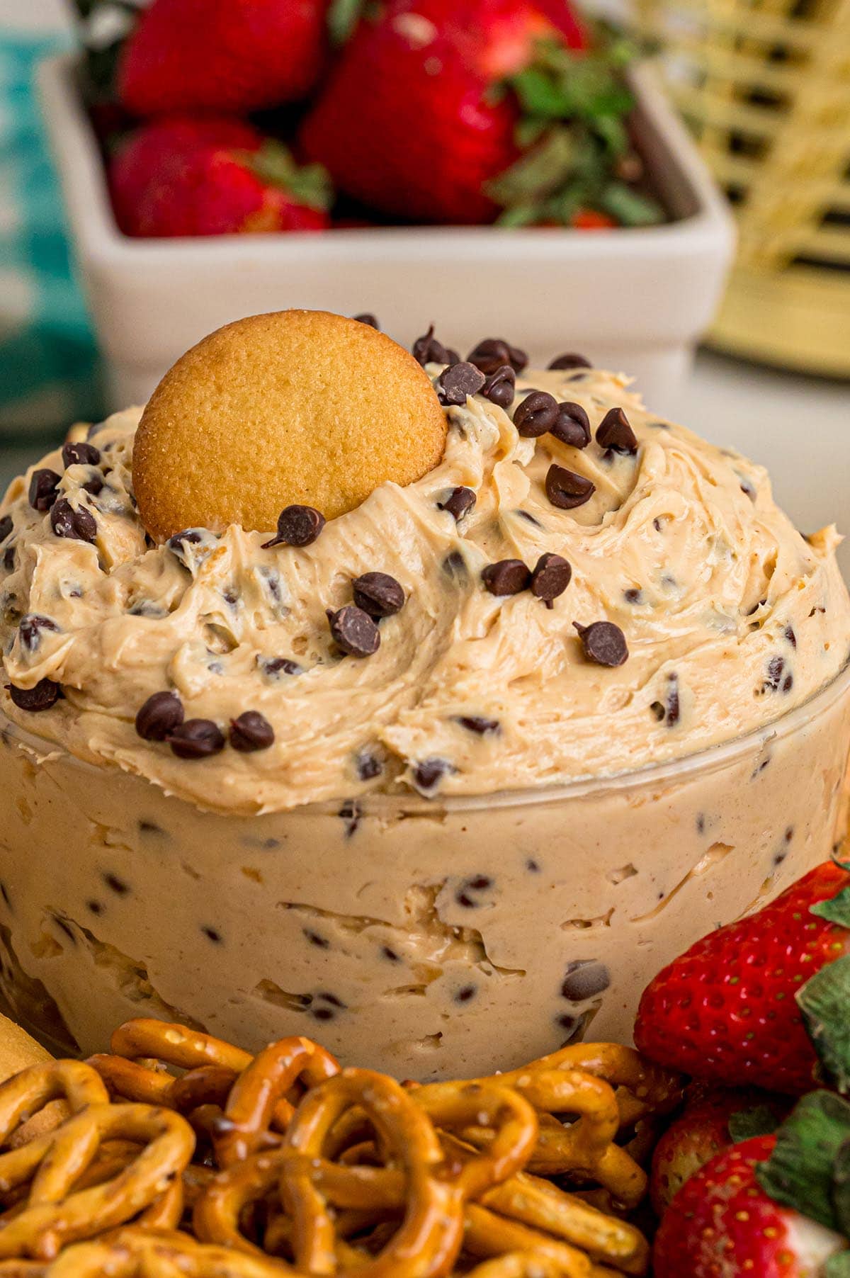 Buckeye dip in a clear bowl with chocolate chips and a cookie on top, strawberries and pretzels around it.