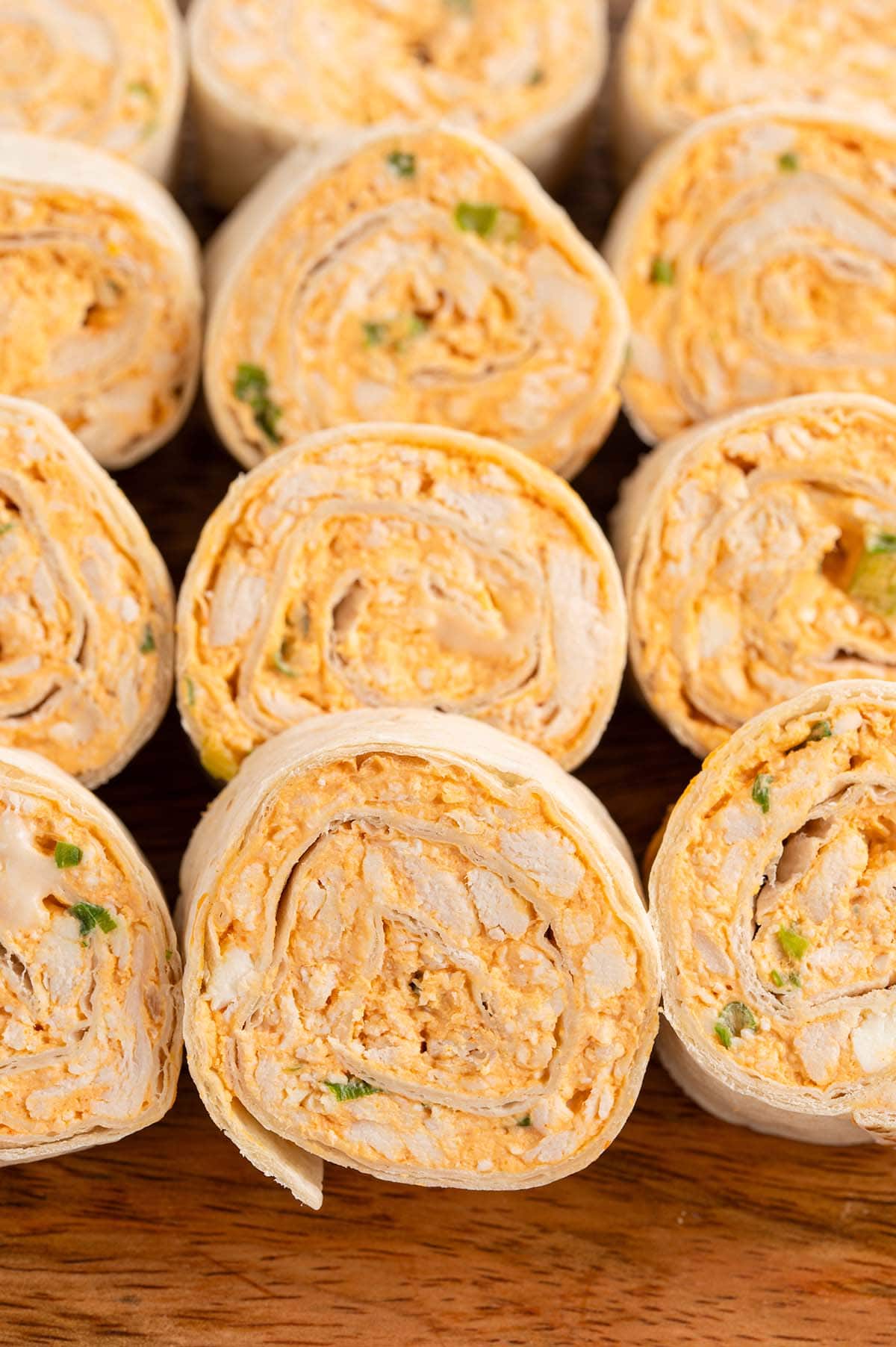 Buffalo chicken pinwheels sliced and stacked on a wood board.