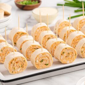 Buffalo chicken pinwheels on toothpicks in a white tray, with ranch dip and green onions nearby.