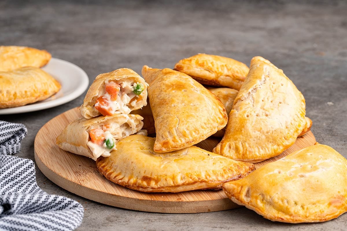 A pile of chicken pot pie hand pies on a circle wooden board