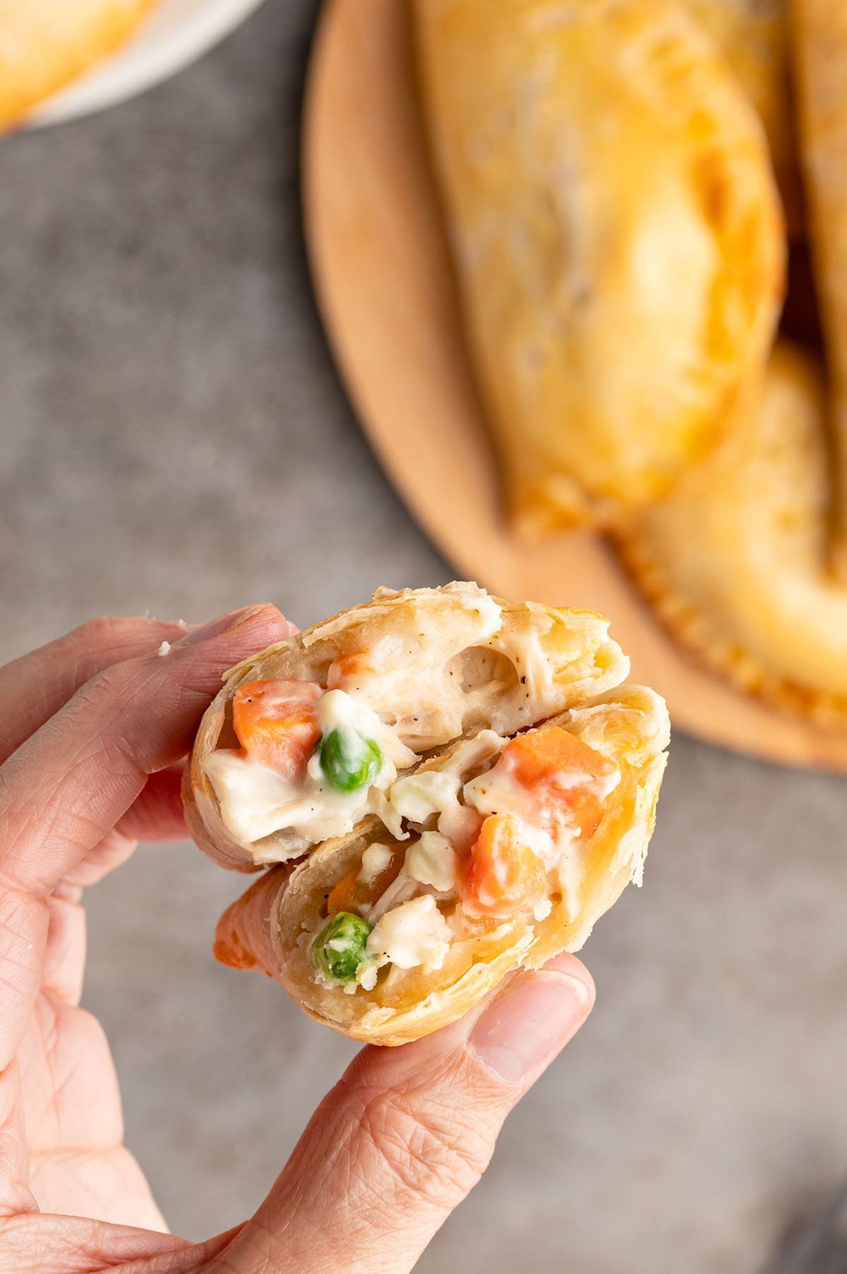 Hand holds open chicken pot pie hand pie with creamy chicken, carrots, and peas.