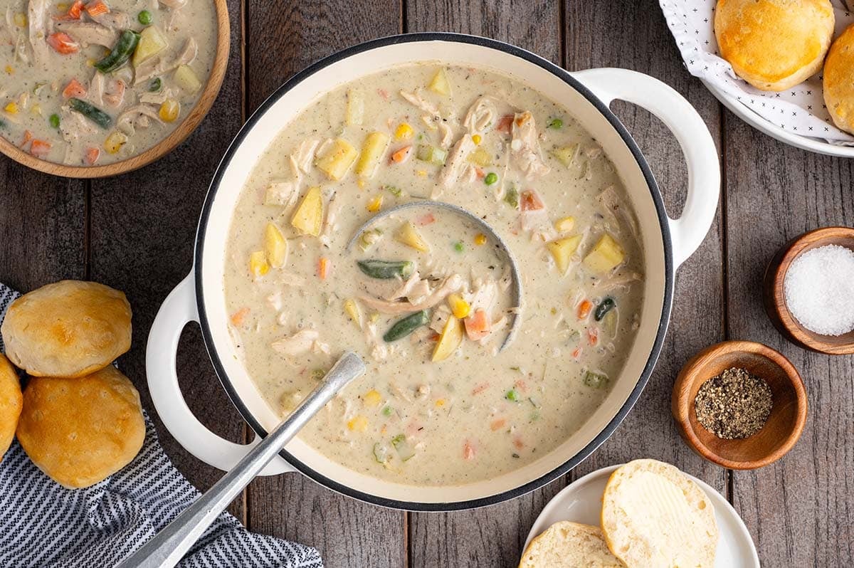 Creamy chicken pot pie soup in a white pot with chicken chunks, potatoes, corn, peas, and carrots.
