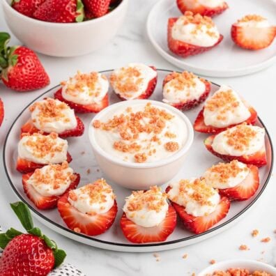 Halved strawberries filled with white cream and topped with golden crumbs, arranged in a circle on a white plate.
