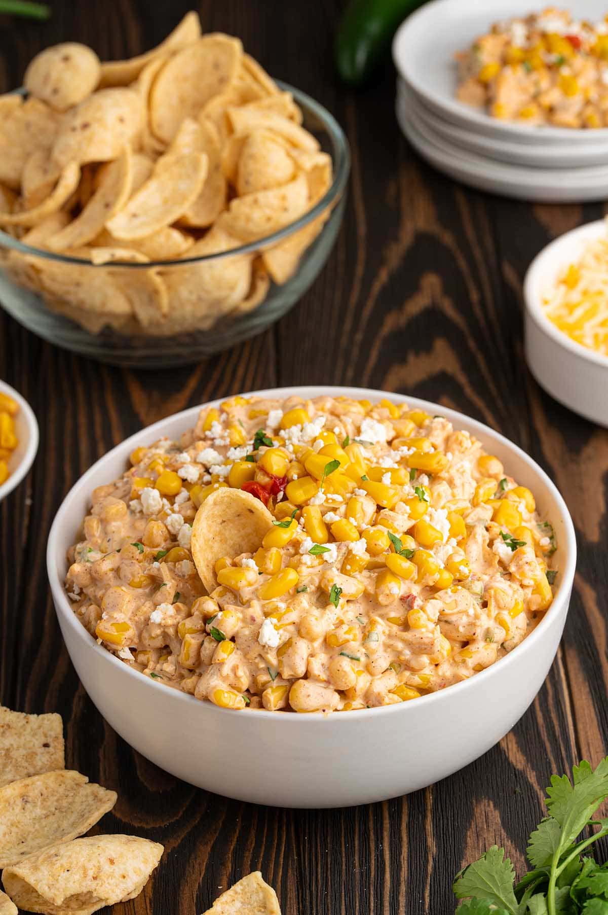 Bowl of Mexican street corn dip topped with cotija cheese, corn kernels, and cilantro next to tortilla chips.