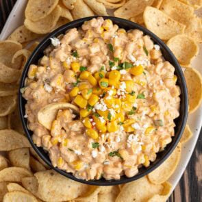 Bowl of creamy Mexican street corn dip with corn kernels, cotija cheese, and cilantro, next to tortilla chips.