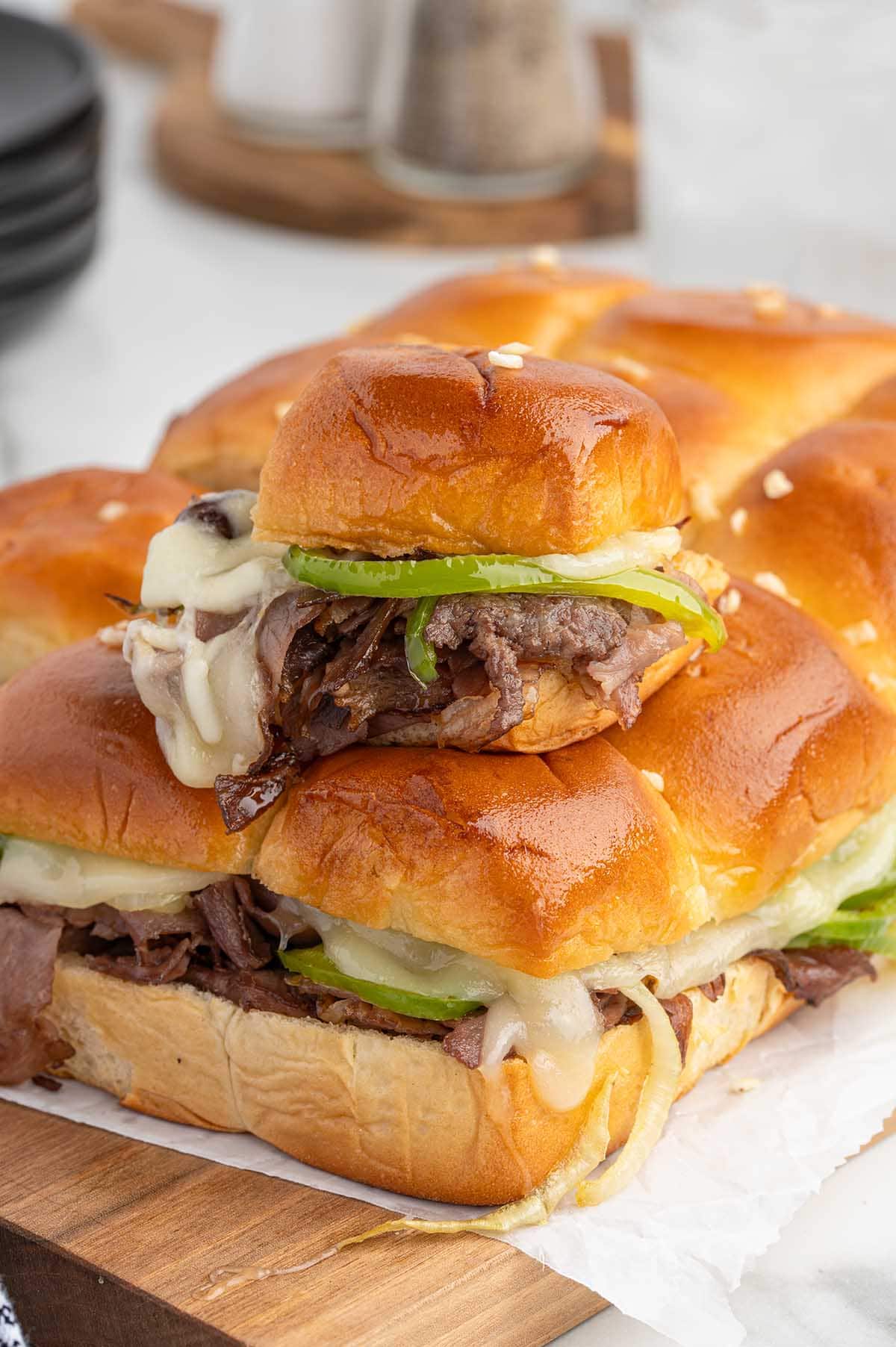 Stack of Philly cheesesteak sliders with melted cheese, beef, and green peppers on soft buns.