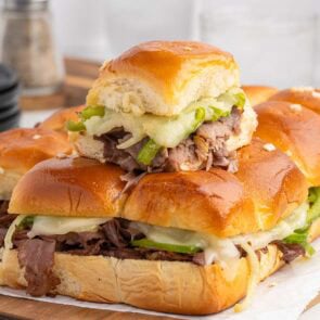 Stack of Philly cheesesteak sliders with melted cheese, green peppers, and tender beef on soft buns.