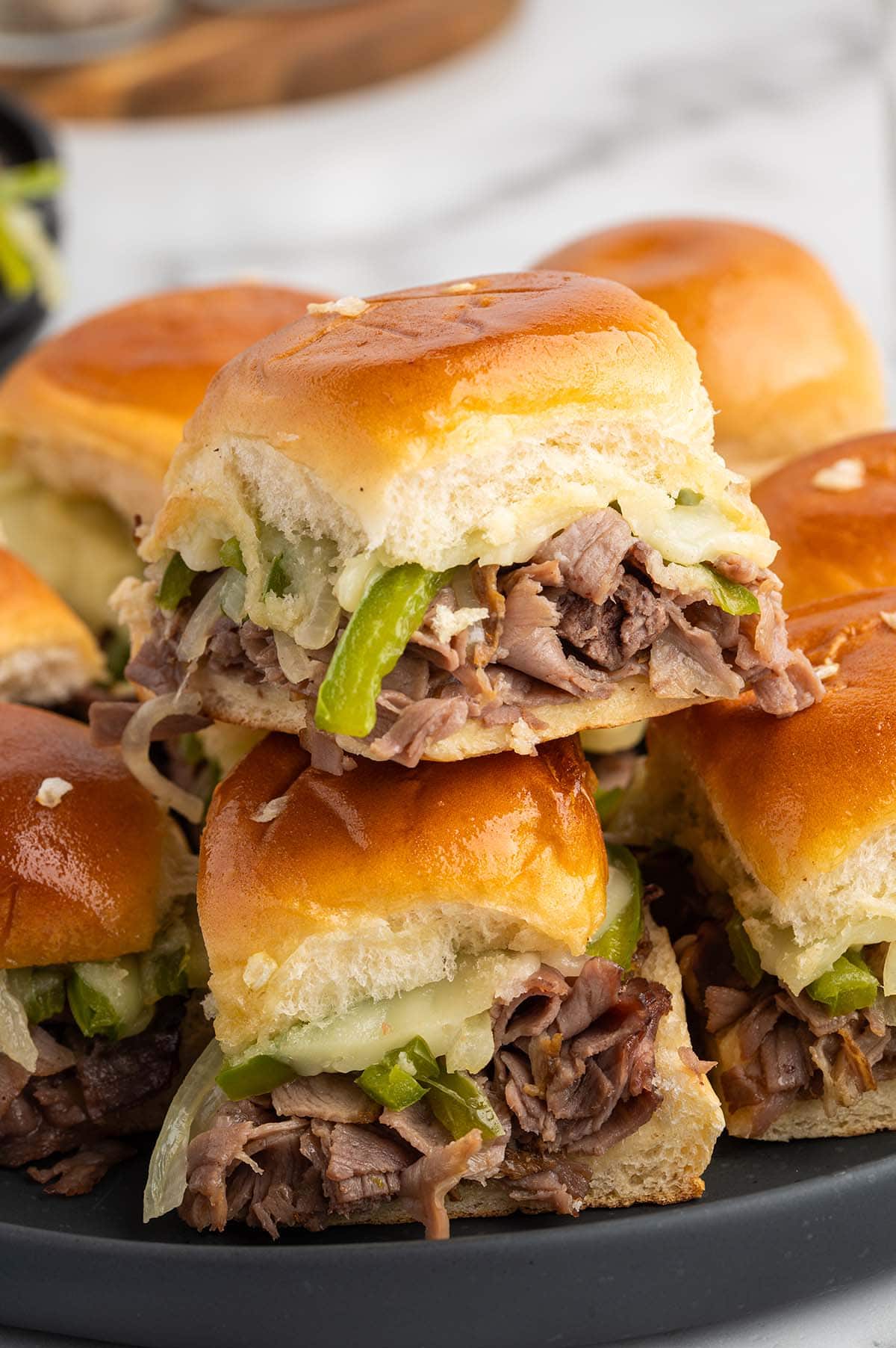 Stack of golden Philly cheesesteak sliders topped with melted cheese and peppers.
