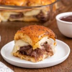 Mini roast beef sandwich topped with cheese sits on a white plate.